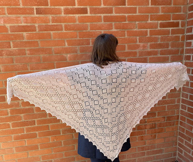 Vingspannet av en stor ljusgrå spetsstickad sjal.