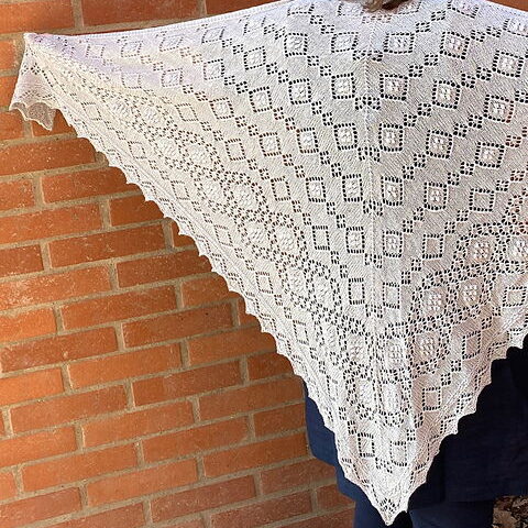 En stor spetsstickad ljust grå sjal.